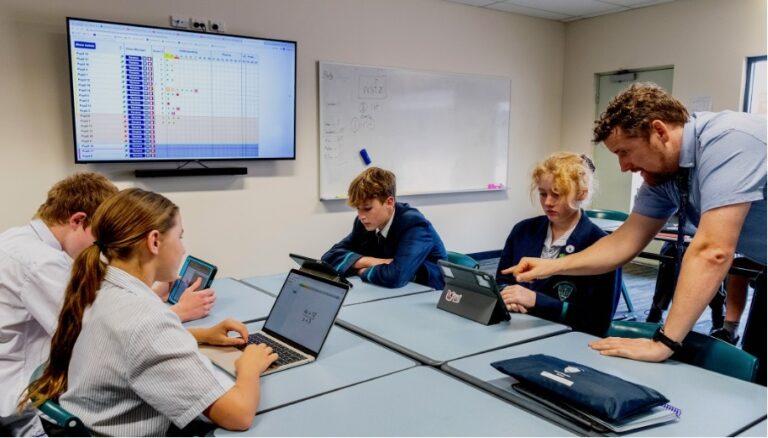 Students working on laptops with a teacher in a classroom