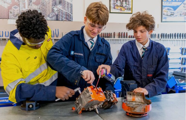 Students in overalls working on a small engine in the automotive workshop