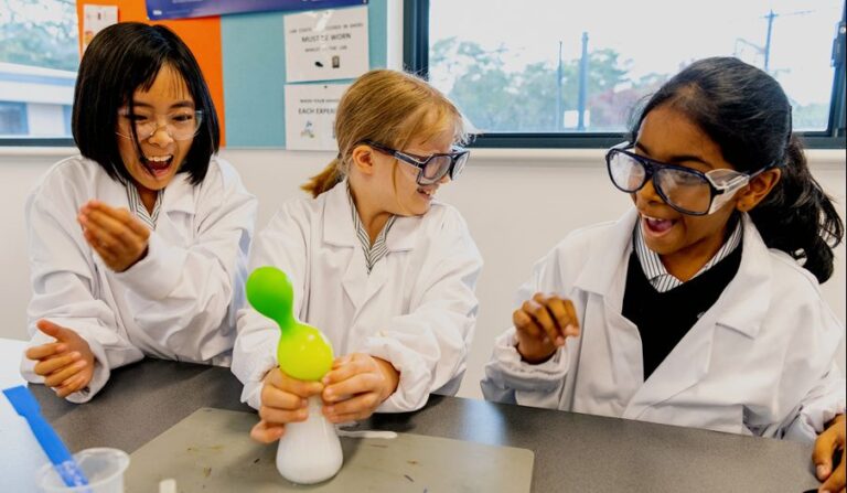 Primary students in lab coats smiling during a science experiment