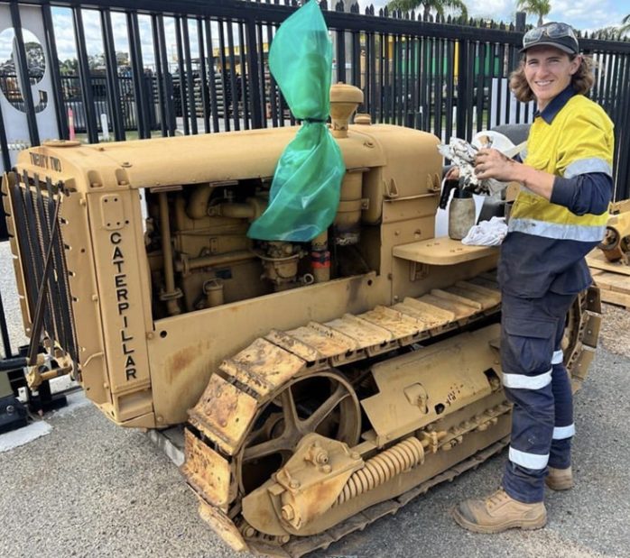 Student in hi-vis inspecting a vintage crawler tractor